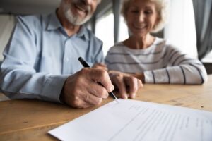 Photo of an elderly couple sitting at a table signing documents and smiling. 