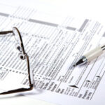 Tax forms and a pen arranged neatly on a wooden desk, ready for completion and submission.
